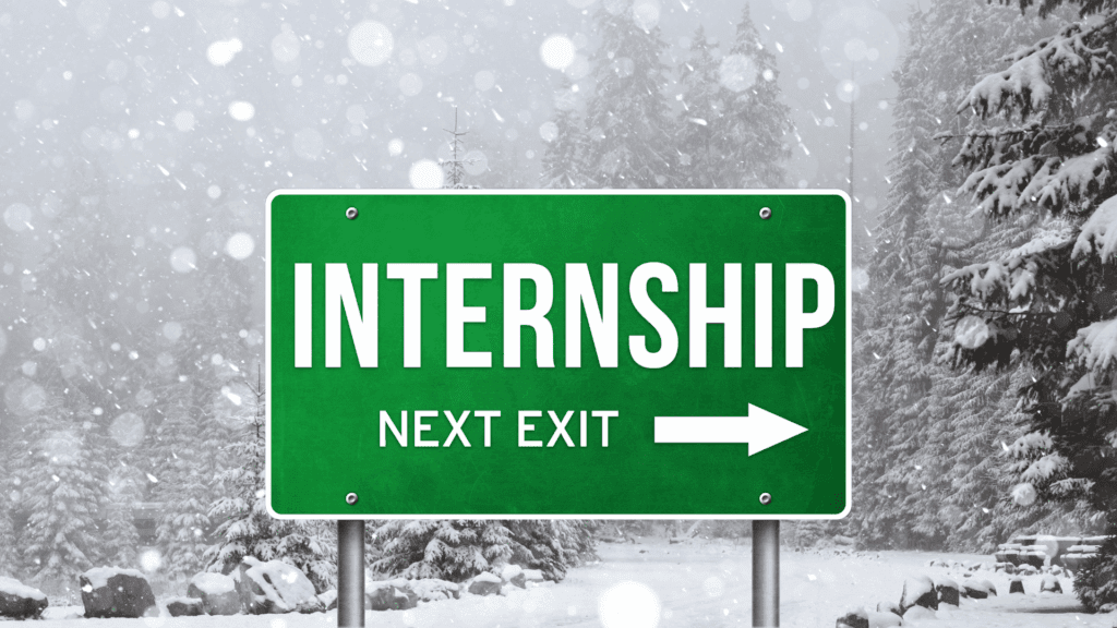Green highway sign reading ‘Internship Next Exit’ on a snowy winter road, symbolizing opportunities for paid winter internships.