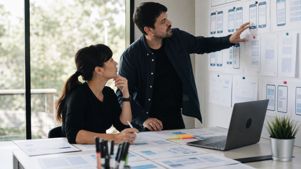 Two adult volunteers leading an accessible interface-design review using abstract wireframes without readable text or student information.